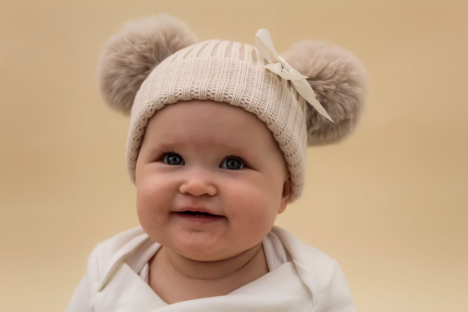 Neutral knitted baby hat with pom poms and bow