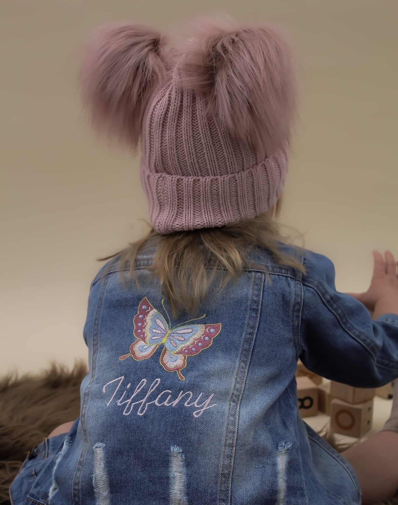 Butterfly embroidered denim jacket with rose gold double pom pom knitted hat